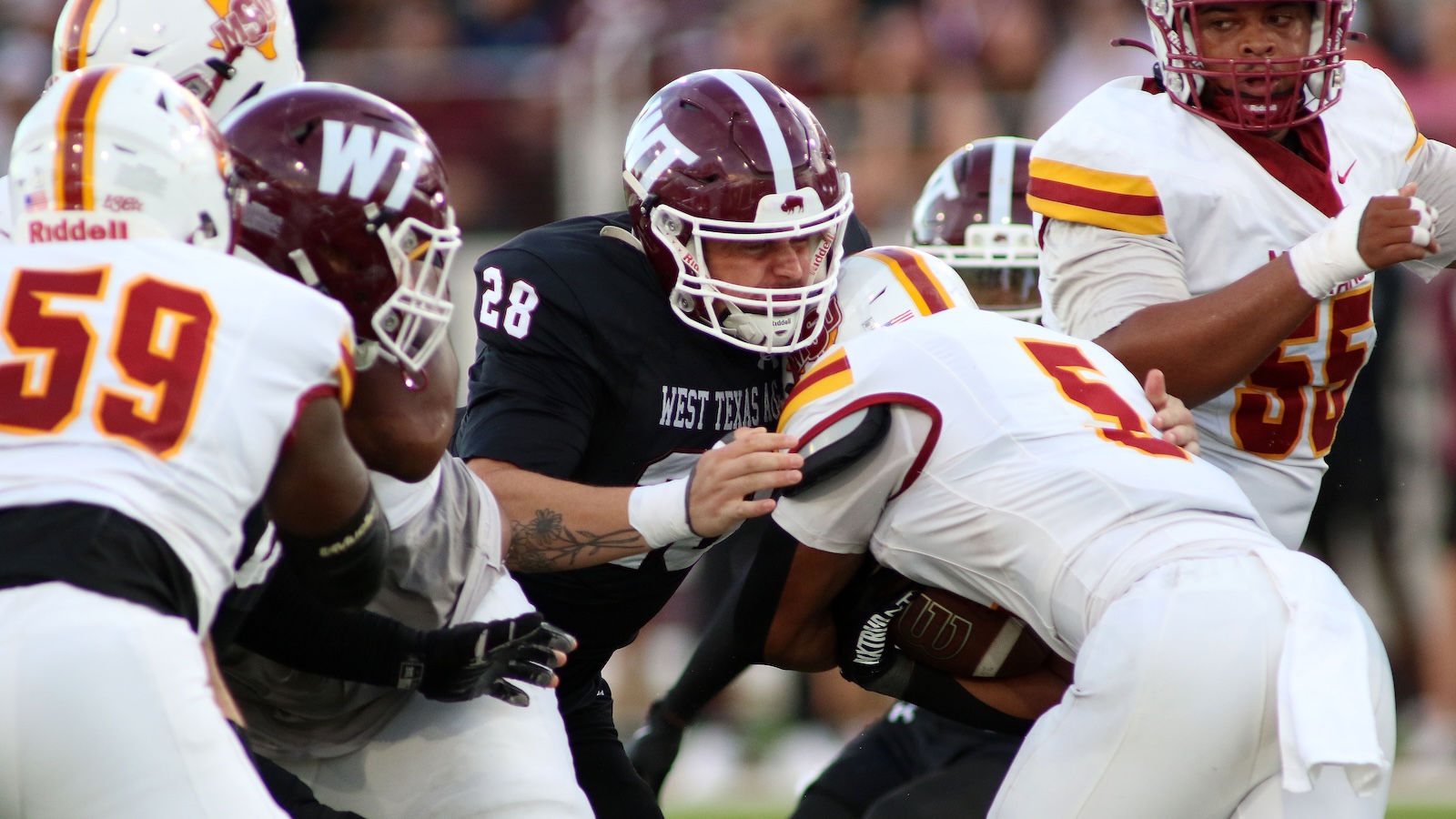 West Texas A&M defender #28 engages a ball carrier as players clash on a college football field.