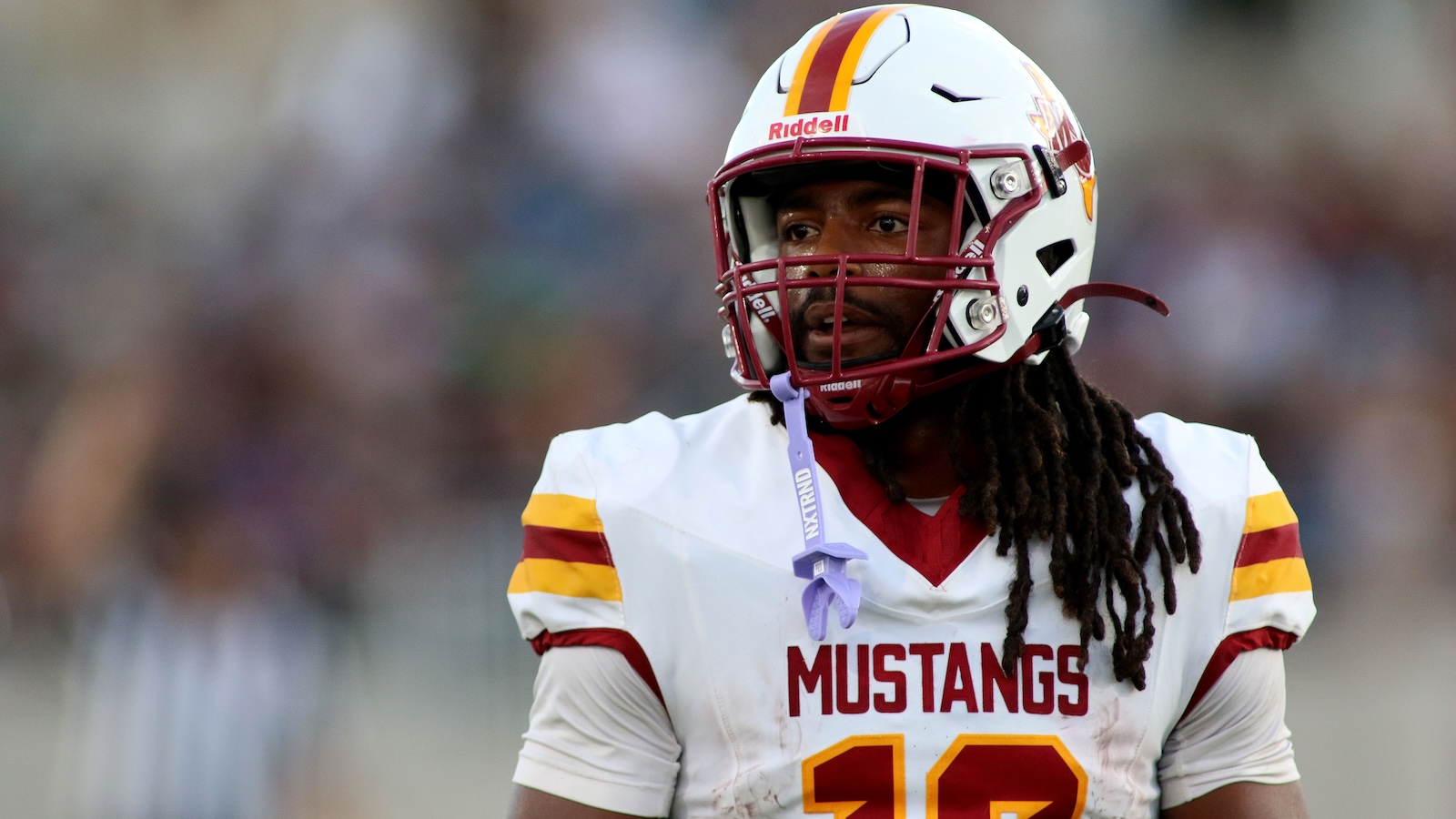 American football player in a white Mustangs jersey with maroon and gold accents, number 10, helmet on, looking to the side on the field.