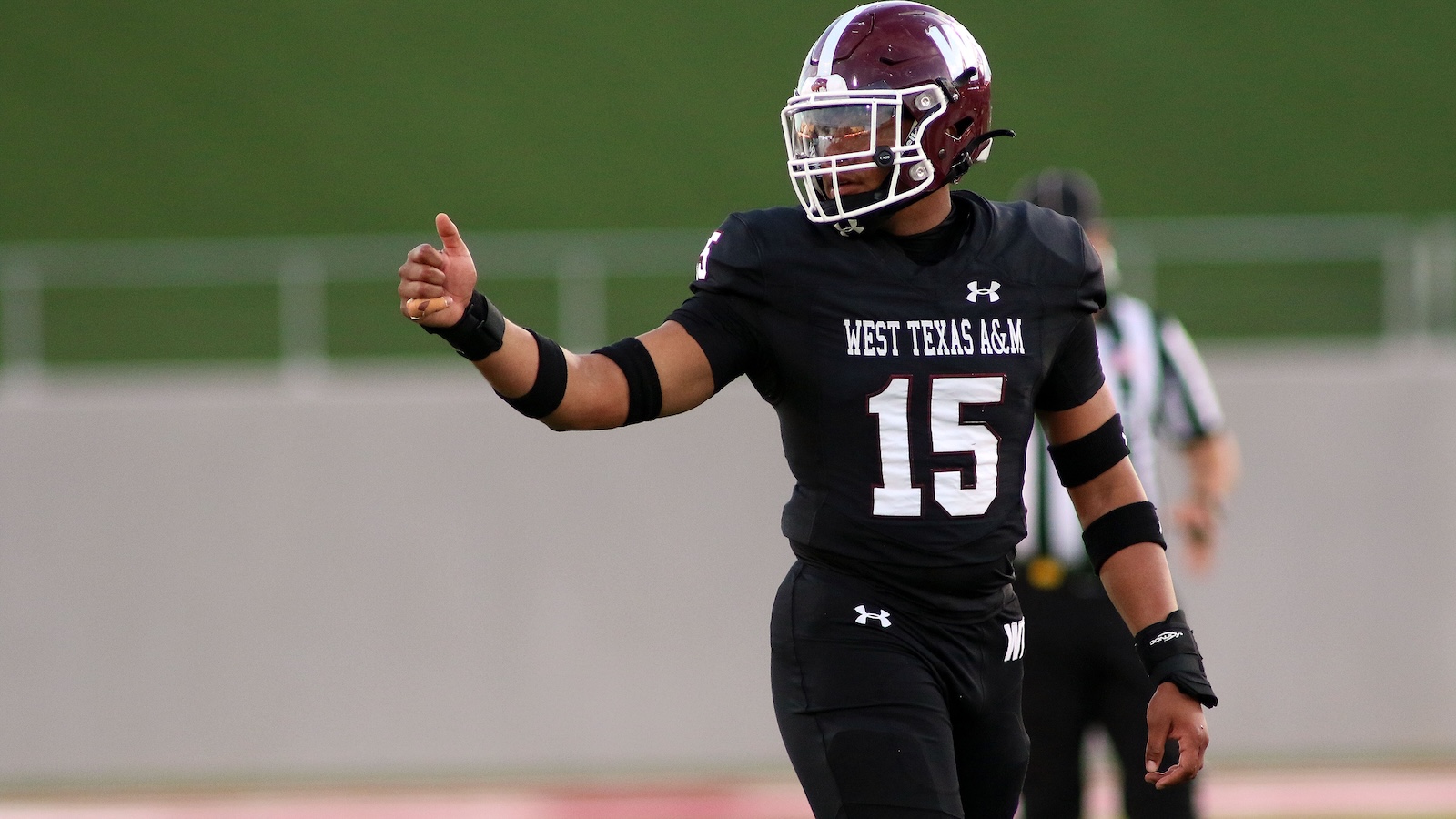 West Texas A&M football player #15 gives a thumbs-up on the field, helmet on and uniform dark color.