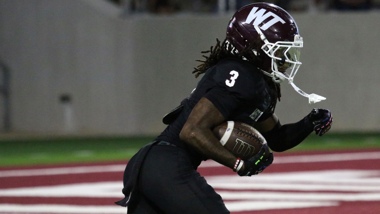 Football player in black jersey #3 runs with the ball during a game, night field.