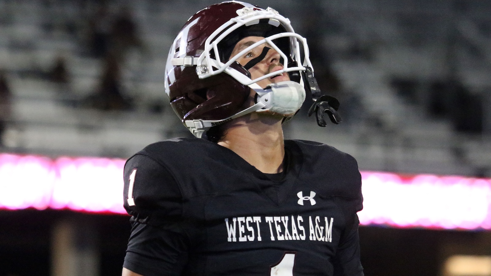 Football player in a black West Texas A&M uniform with the number 1, wearing a white helmet and looking upward on the field.