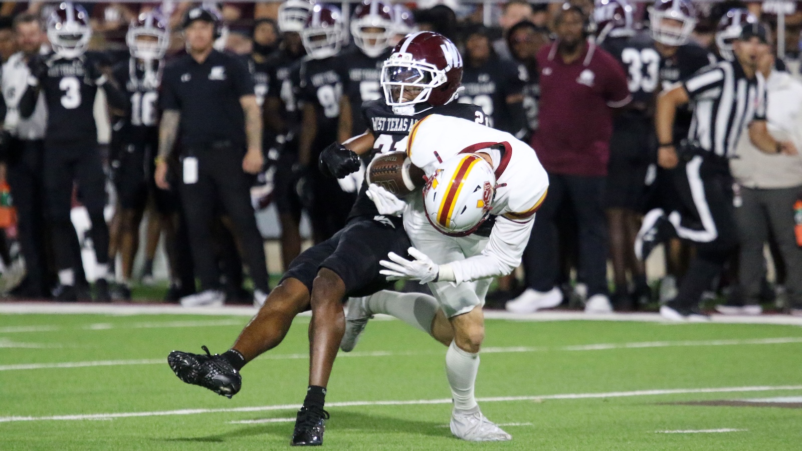Black-jersey defender tackles a white-jersey ball carrier on a football field.