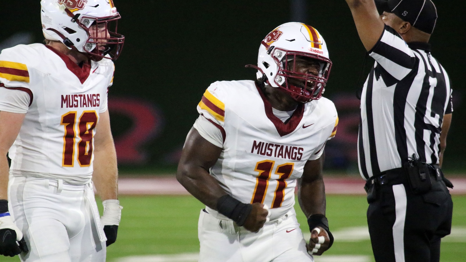 Two Mustangs football players in white jerseys with maroon and gold numbers, facing a referee with arms raised.