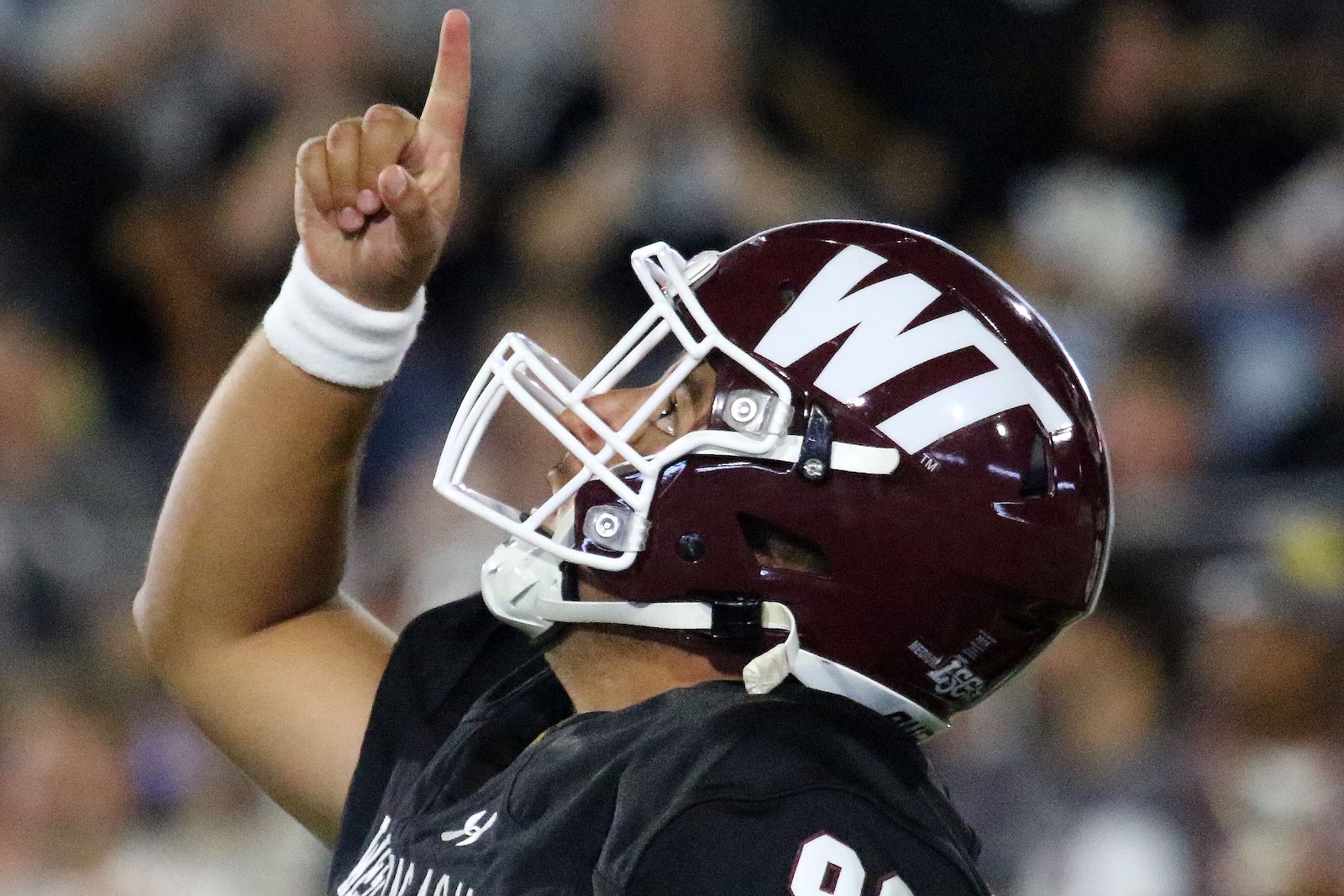 Football player wearing maroon helmet raises one finger in victory gesture.