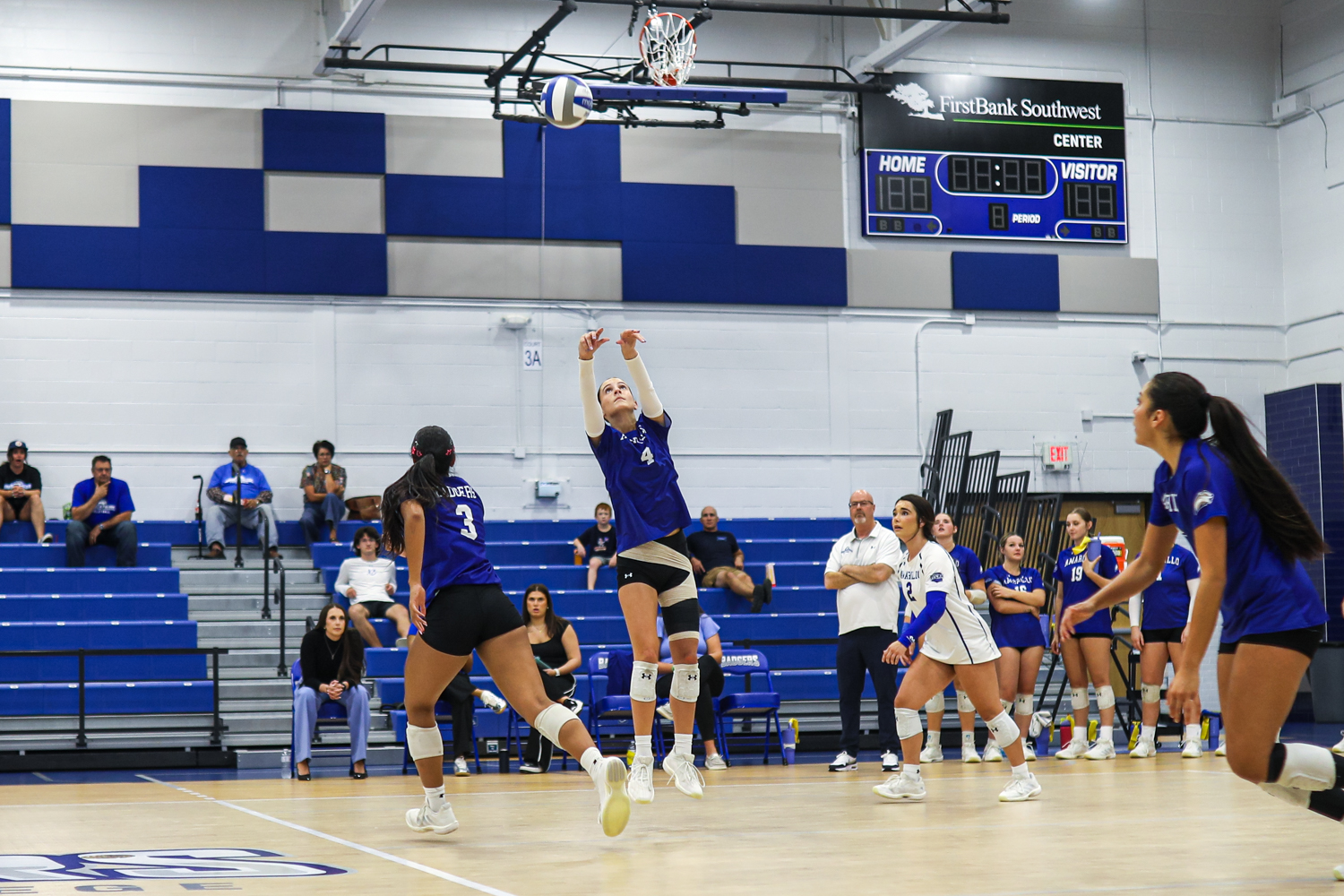 Edit 4 1 | Press Pass Sports Blue team player (number 4) leaps to hit the ball as others watch on a gym court during a volleyball match.