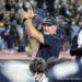 20260828-AmarilloHigh-PaloDuro-FB-045 | Press Pass Sports Man in a dark shirt and cap claps his hands in celebration on a sports field, with cheering spectators blurred in the background.