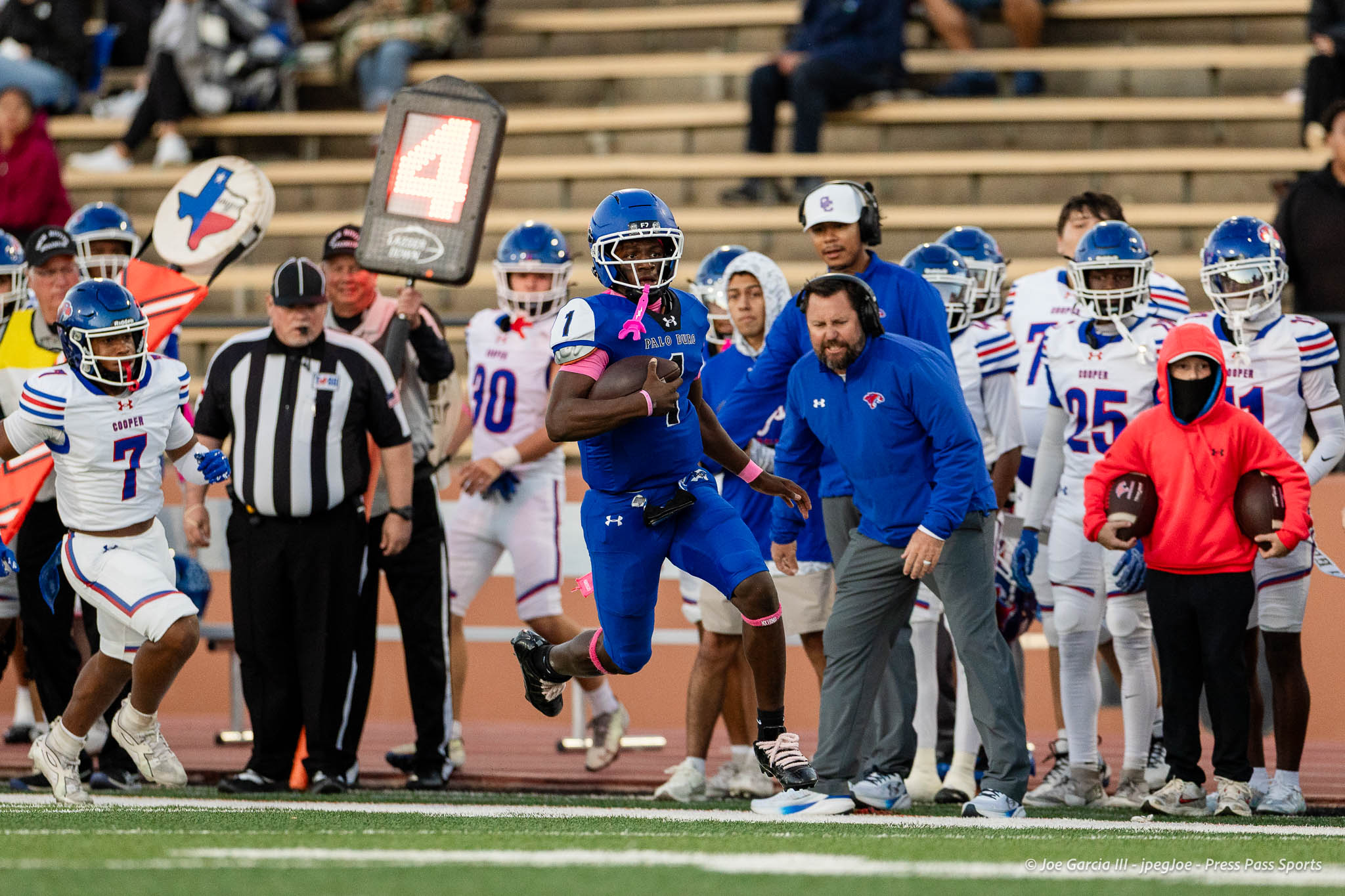 abilene-cooper-vs-palo-duro-jpegJoe-pps-7 | Press Pass Sports A football player in blue runs with the ball on the field while teammates and a coach watch from the sideline in the background.