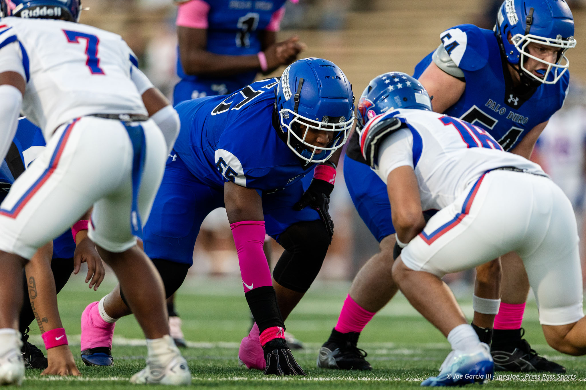 abilene-cooper-vs-palo-duro-jpegJoe-pps-8 | Press Pass Sports Football players in blue and white uniforms engage at the line of scrimmage during a play on a green field.