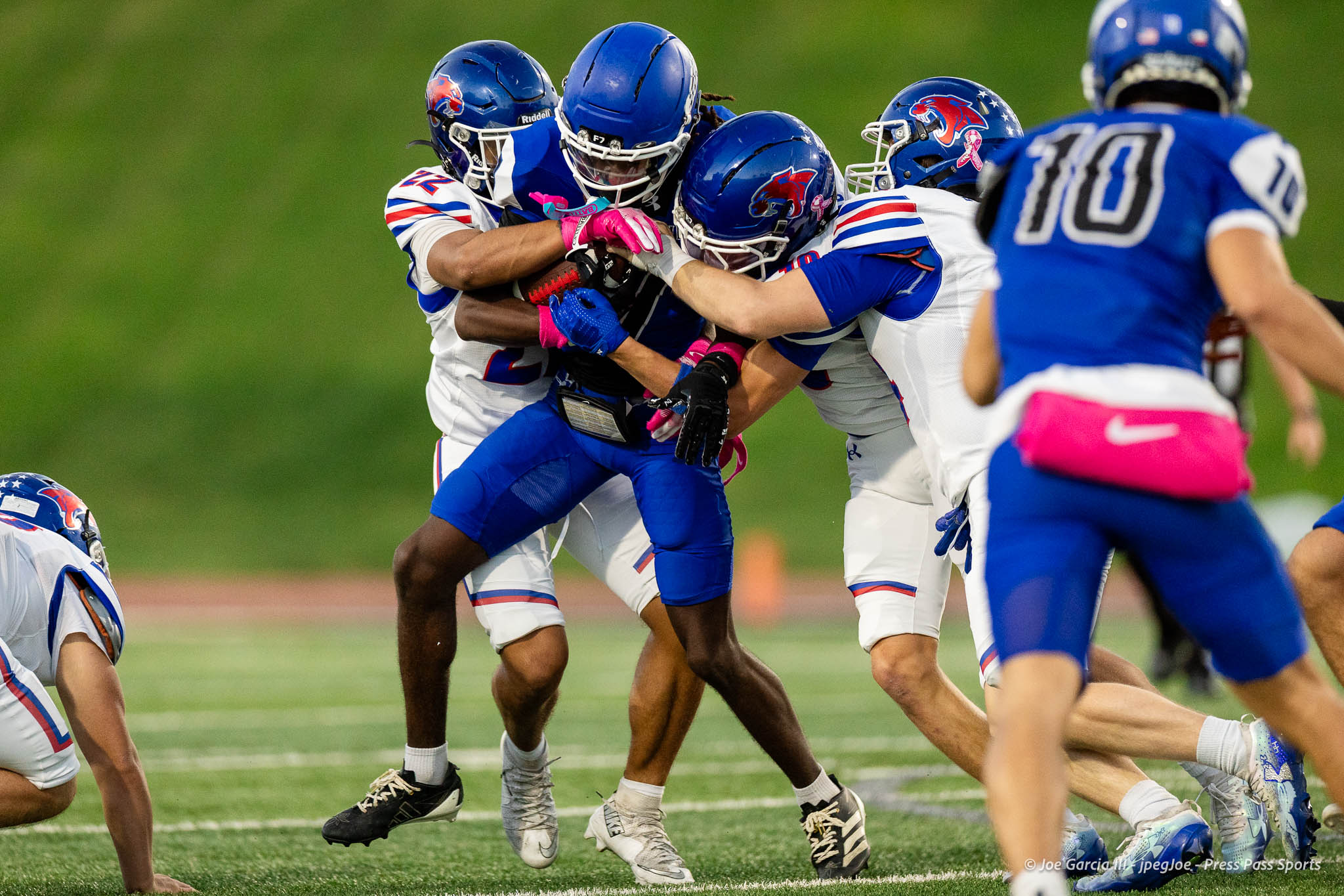 abilene-cooper-vs-palo-duro-jpegJoe-pps-9 | Press Pass Sports Group of football players in blue and white uniforms pile up and tackle on a green field during a game.