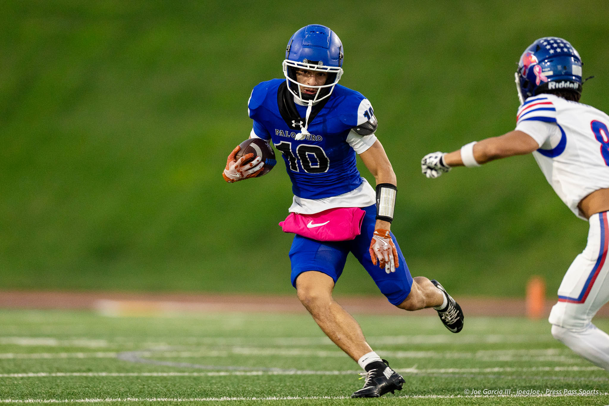 abilene-cooper-vs-palo-duro-jpegJoe-pps-10 | Press Pass Sports A football runner in a blue jersey with the ball powers forward as a white-uniform defender closes in on a green field.