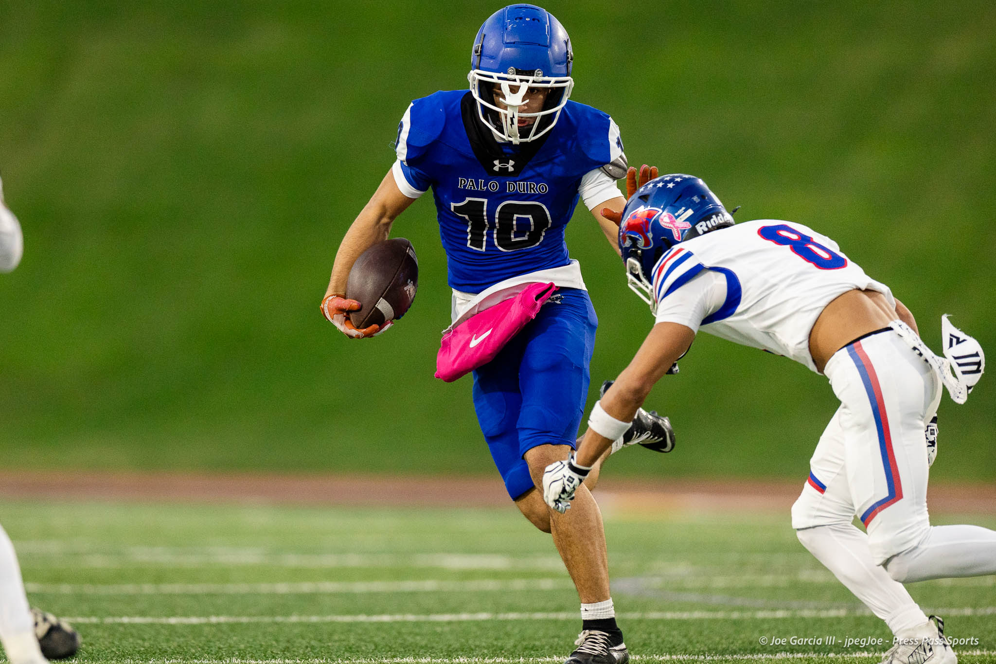 abilene-cooper-vs-palo-duro-jpegJoe-pps-11 | Press Pass Sports Football player in a blue uniform (number 10) runs with the ball, pursued by a defender on a green field.