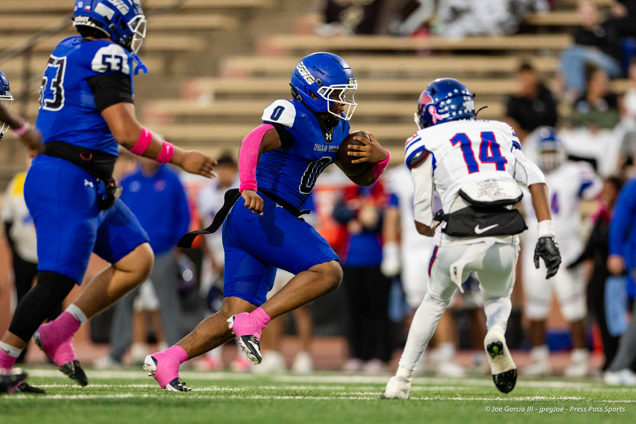 abilene-cooper-vs-palo-duro-jpegJoe-pps-12 | Press Pass Sports Blue-jersey football player runs with the ball, pursued by a white-jersey defender on a green turf field.