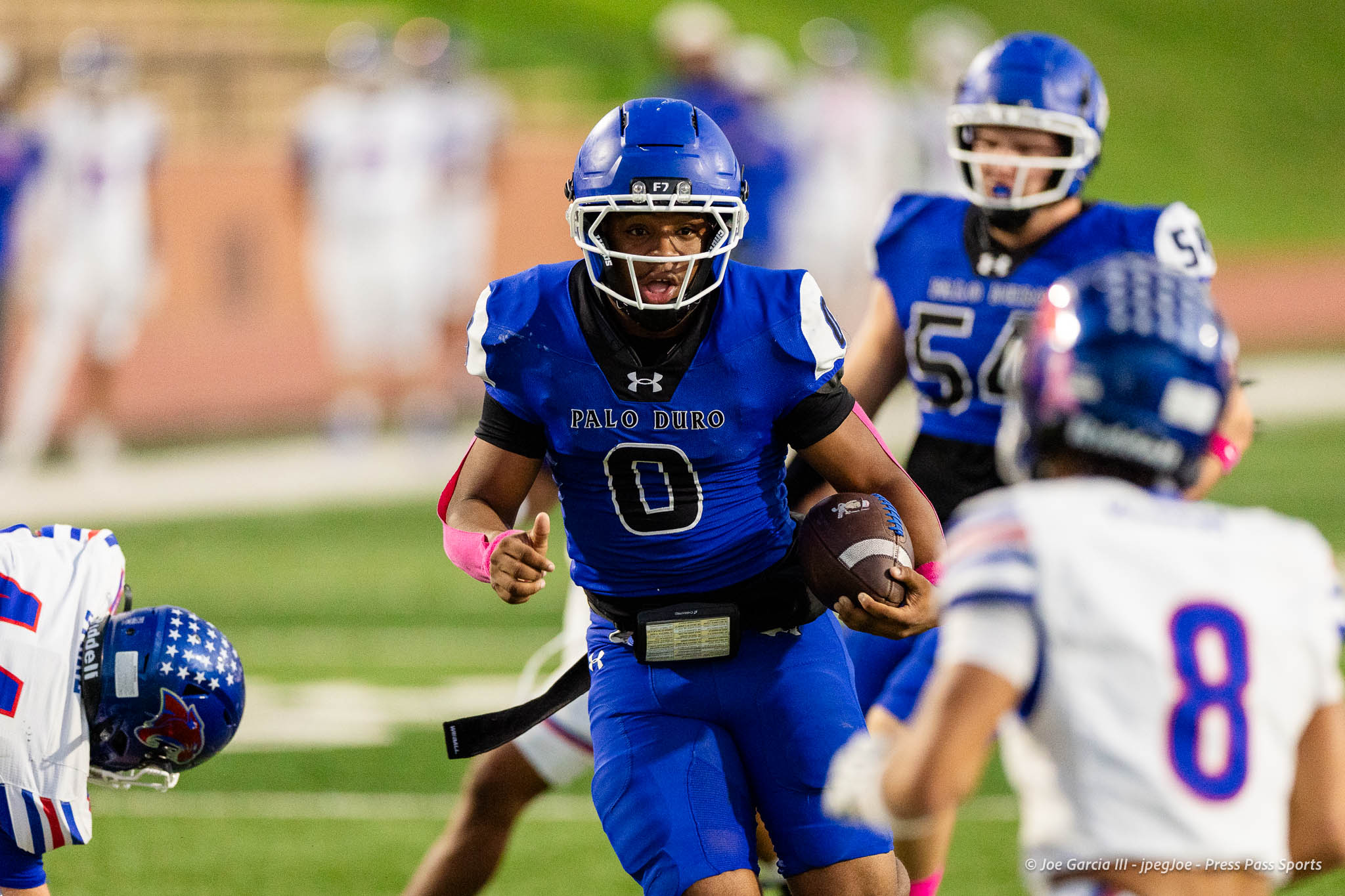 abilene-cooper-vs-palo-duro-jpegJoe-pps-15 | Press Pass Sports Palo Duro football player in blue jersey (#0) running with the ball during a game, teammates and defenders blurred in the background on a green field.