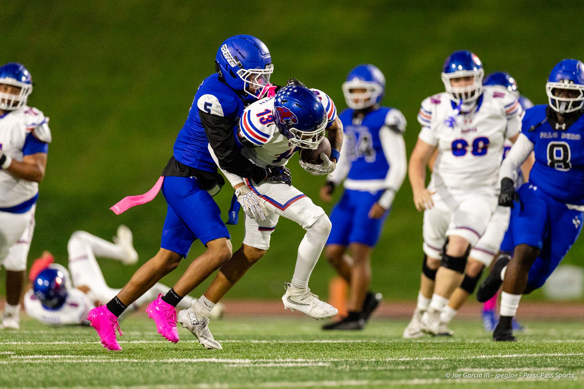 abilene-cooper-vs-palo-duro-jpegJoe-pps-16 | Press Pass Sports Football players in blue and white uniforms collide during a night game as a defender tackles a ball carrier.