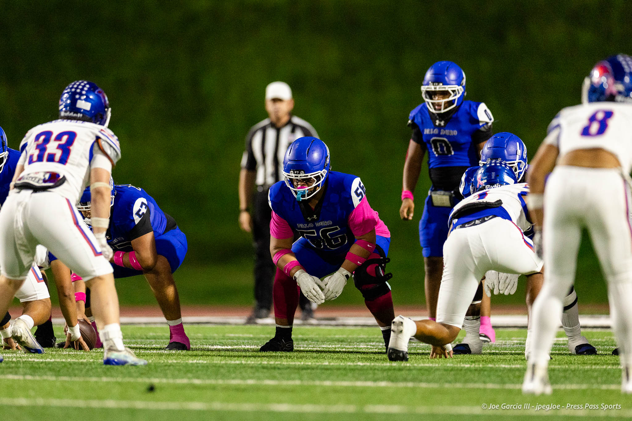abilene-cooper-vs-palo-duro-jpegJoe-pps-17 | Press Pass Sports Football game action on a night game: blue-team players near the line of scrimmage with a referee in the background.