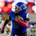 abilene-cooper-vs-palo-duro-jpegJoe-pps-18 | Press Pass Sports American football player in a blue uniform runs with the ball during a game, pink wristbands visible on his arms.