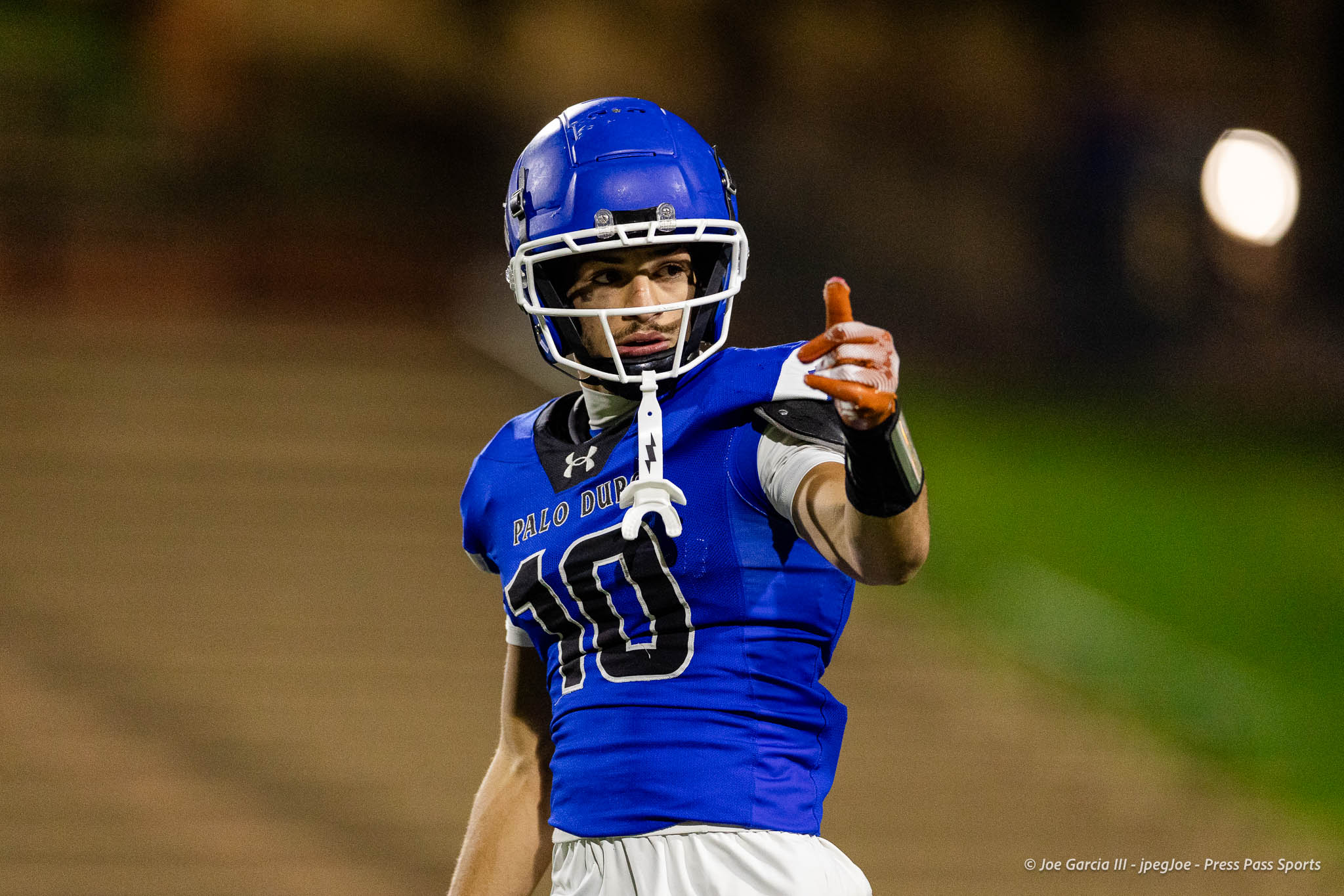abilene-cooper-vs-palo-duro-jpegJoe-pps-19 | Press Pass Sports Lacrosse player in a blue jersey and white helmet pointing toward the camera on a field at night/ dusk light.