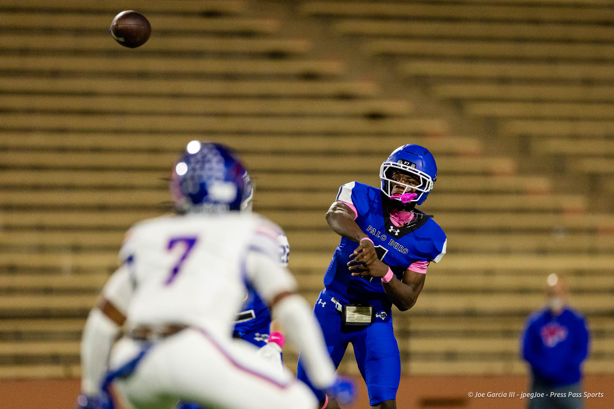 abilene-cooper-vs-palo-duro-jpegJoe-pps-20 | Press Pass Sports Blue football player in a helmet and jersey reaches forward as a ball flies overhead in an indoor stadium; blurred white opponent in the foreground.