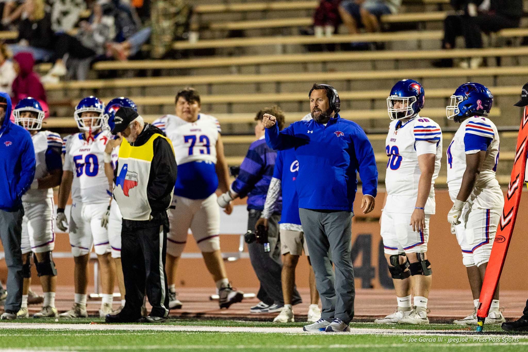 abilene-cooper-vs-palo-duro-jpegJoe-pps-24 | Press Pass Sports Coach in blue jacket pointing as players in white-blue uniforms stand on the sideline during a football game on the field.