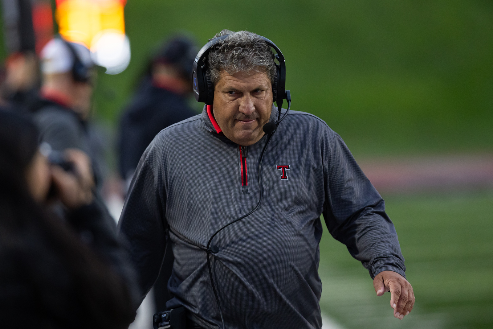THS-AHS-FB-8 | Press Pass Sports Football coach wearing a headset and gray zip-neck pullover with a red trim, walking along the sideline.