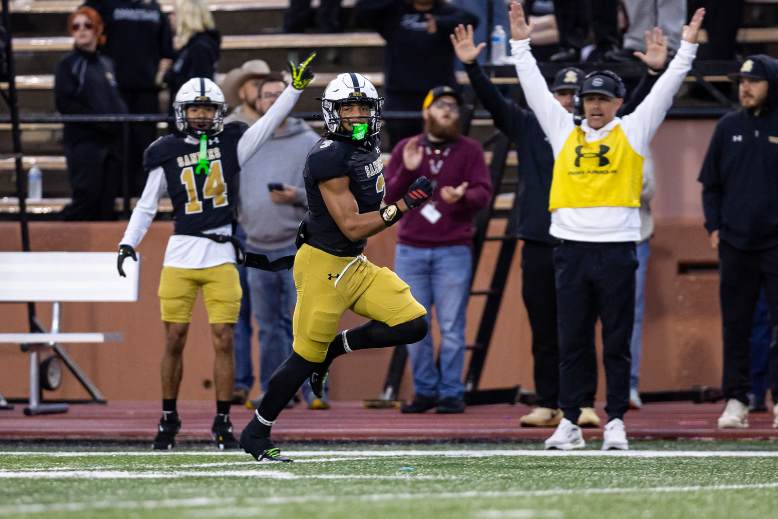 THS-AHS-FB-9 | Press Pass Sports Football player in black and gold runs with the ball as fans cheer in the stands behind him.