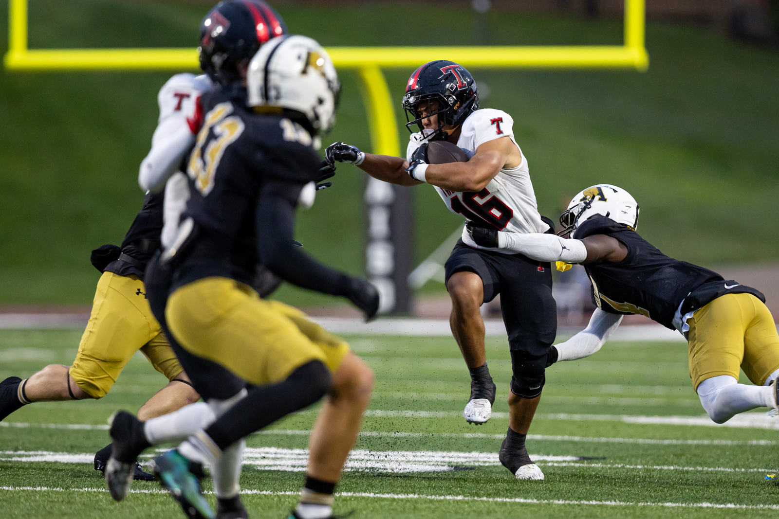 THS-AHS-FB-14 | Press Pass Sports Football player in white jersey (#25) runs with the ball as defenders close in on a green field with a yellow goalpost in the background.