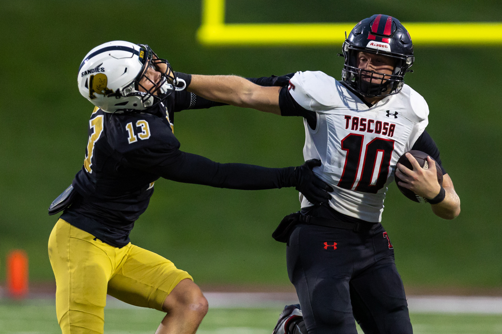 THS-AHS-FB-16 | Press Pass Sports Two football players in mid-action: a white-Tascosa #10 carries the ball while a defender in black and gold reaches in for a tackle.