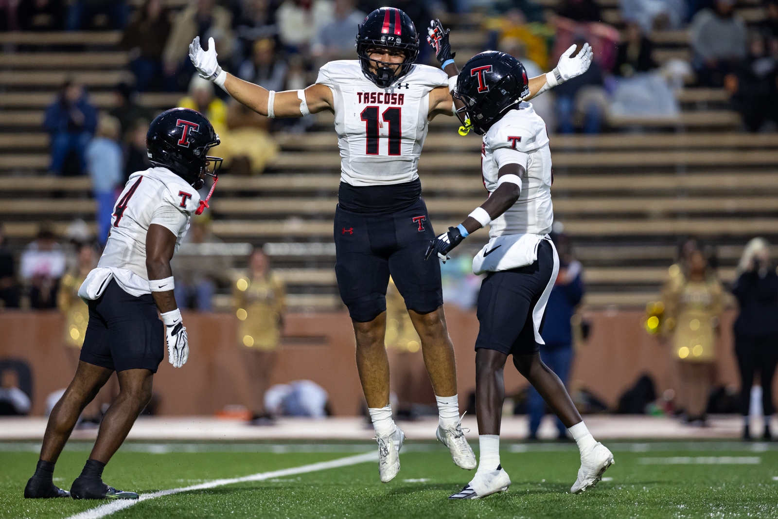 THS-AHS-FB-18 | Press Pass Sports Three Tascosa football players celebrate on the field; center No. 11 leaps with arms raised as teammates approach.