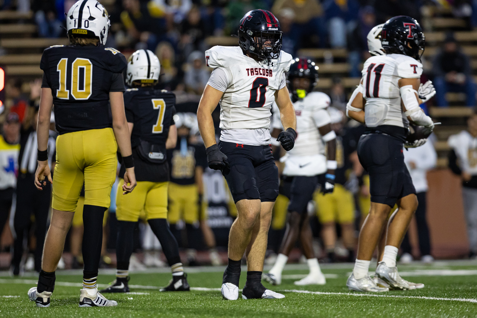 A football player in a white Tasquesa jersey and black shorts stands on the field amid teammates during a game.","Football scene: players in white and navy uniforms gather on the field, two teams facing off.","White-shirt player with number 0 and teammates stand for a moment on a football field during a game.","Group of high school/college football players on the field, preparing for the next play under stadium lights."]} }```Note: The content may be improved with more precise team names if available.```| Incomplete| // Correction: Provide clean JSON. Wait. I'll produce proper array.```{