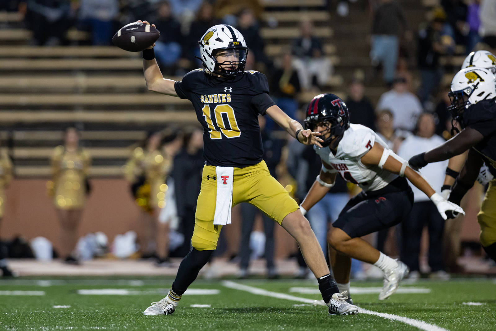 THS-AHS-FB-21 | Press Pass Sports Quarterback in a dark jersey and gold pants (number 10) throws a pass during a football game as defenders close in.