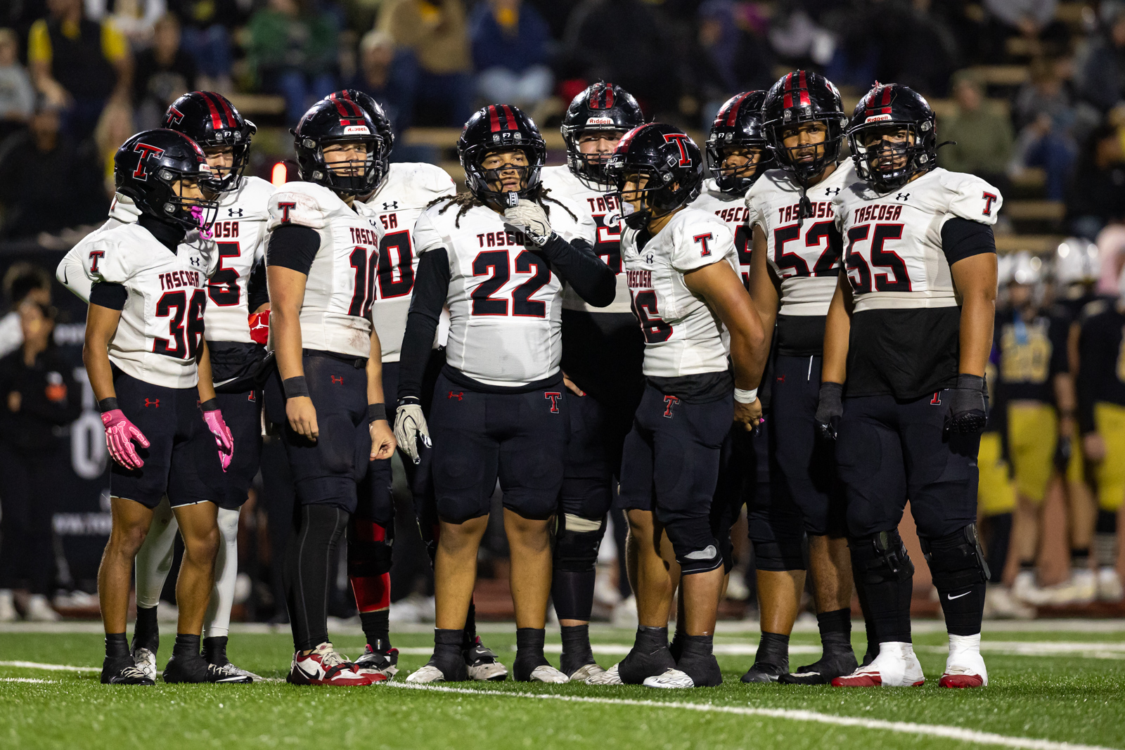 THS-AHS-FB-26 | Press Pass Sports A group of Tasosa football players huddles on a green field in white jerseys with red and black numbers and helmets.