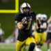 Football player wearing a black jersey (number 7) and yellow pants runs with the ball during a game at night stadium.