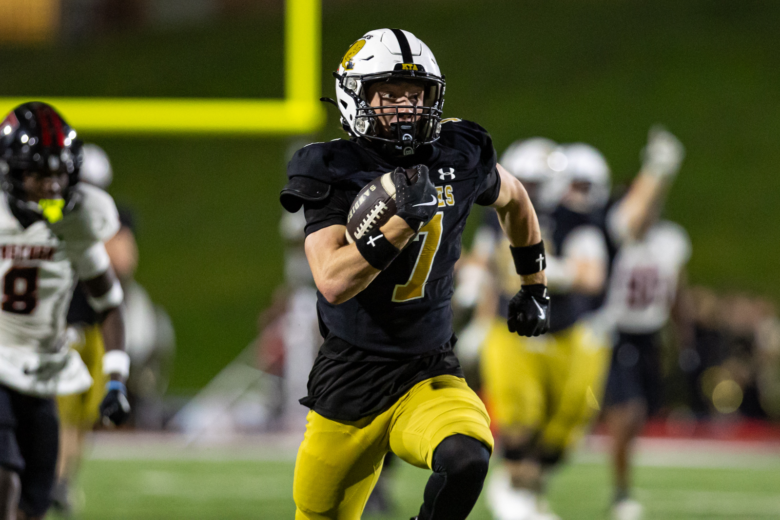 THS-AHS-FB-30 | Press Pass Sports Football player wearing a black jersey (number 7) and yellow pants runs with the ball during a game at night stadium.