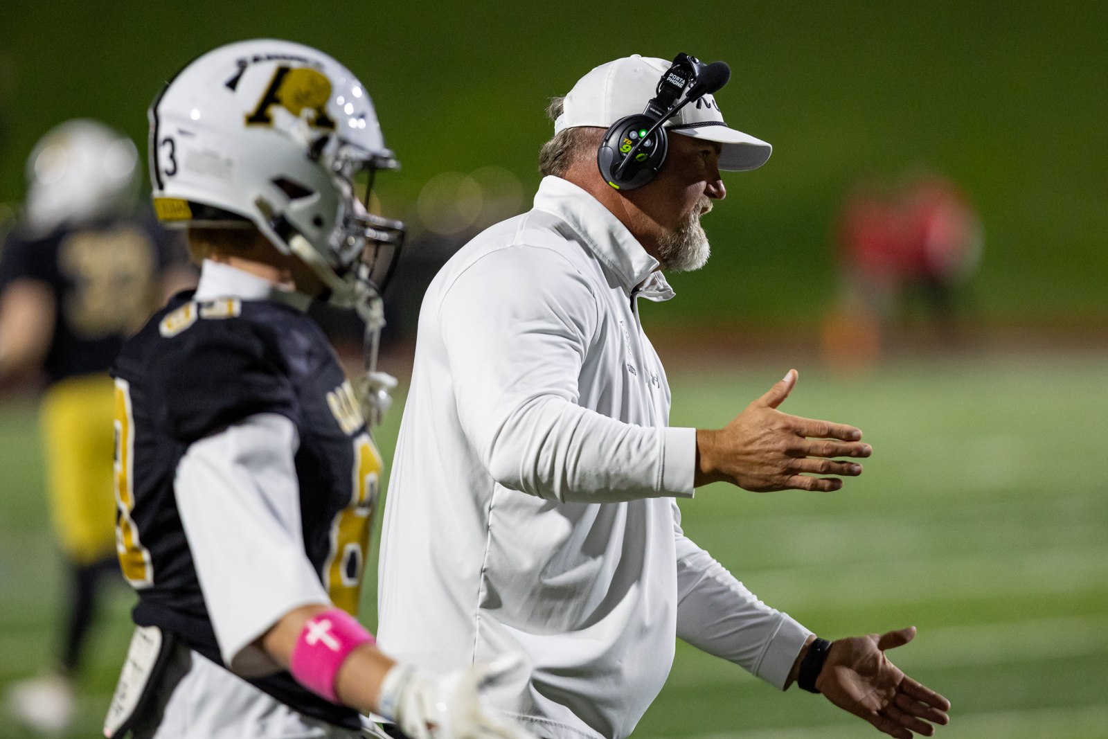 THS-AHS-FB-31 | Press Pass Sports Football coach in a white polo gesturing to players on the sideline during a football game.