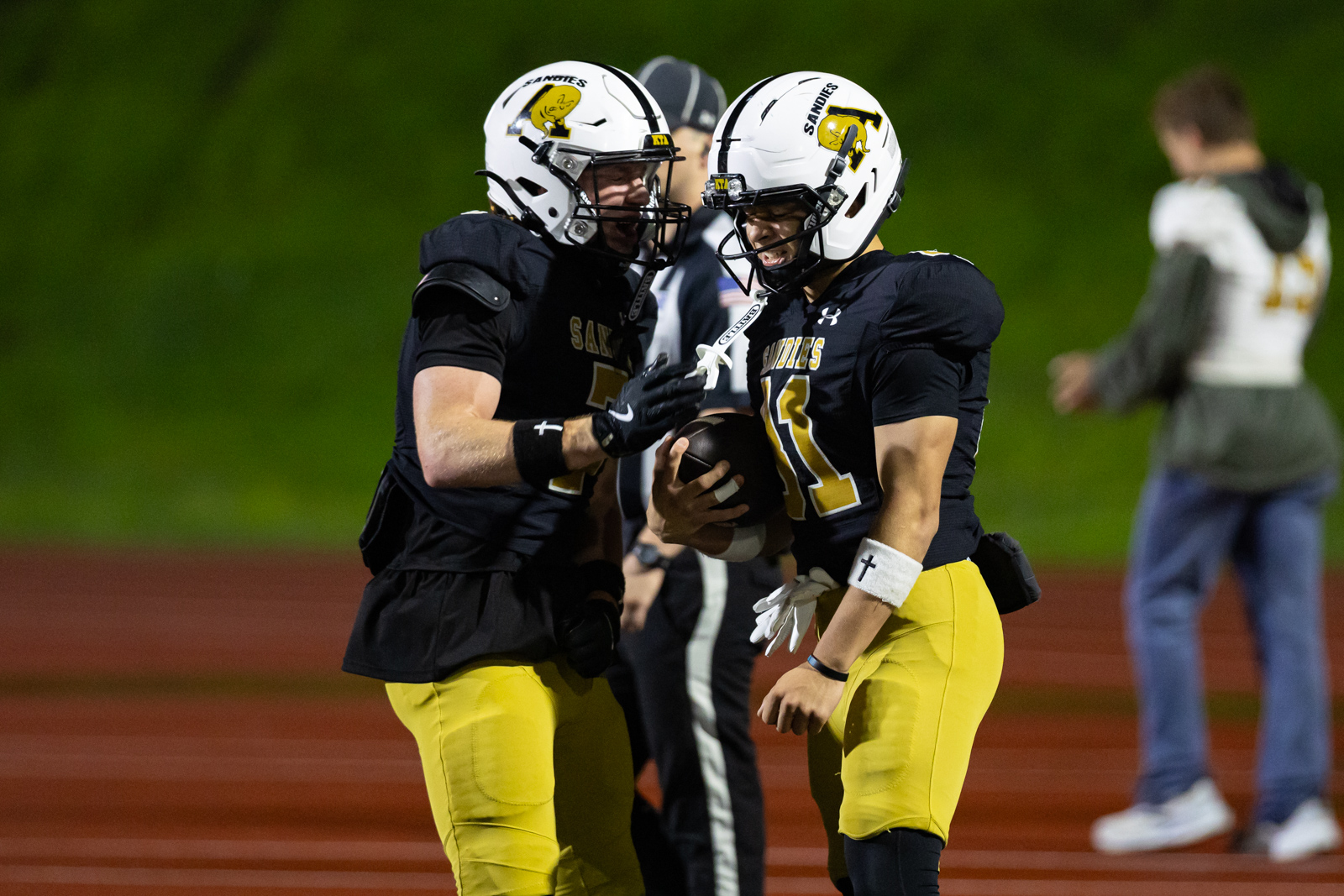 THS-AHS-FB-33 | Press Pass Sports Two football players in black jerseys and yellow pants celebrate on the field, one holding the ball as the other high-fives him.