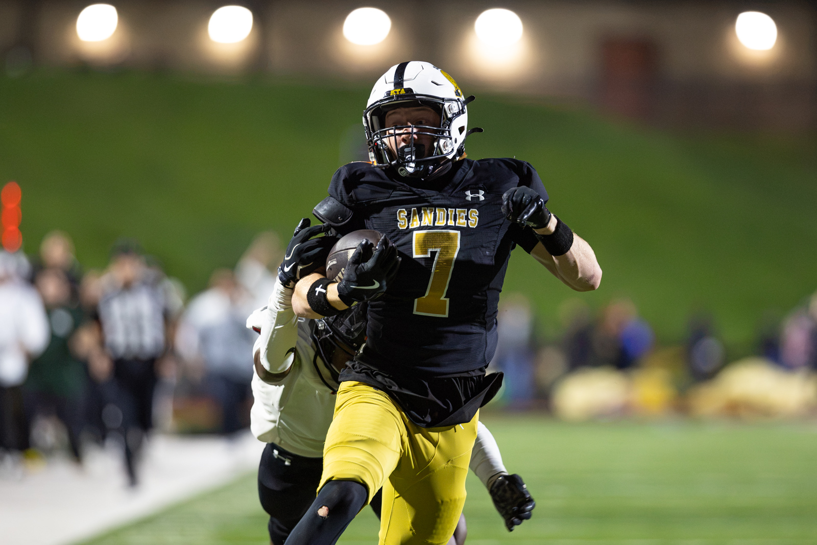 THS-AHS-FB-39 | Press Pass Sports American football player in black and gold (Sandies) jersey with the ball, sprinting toward the end zone at night on a green field.