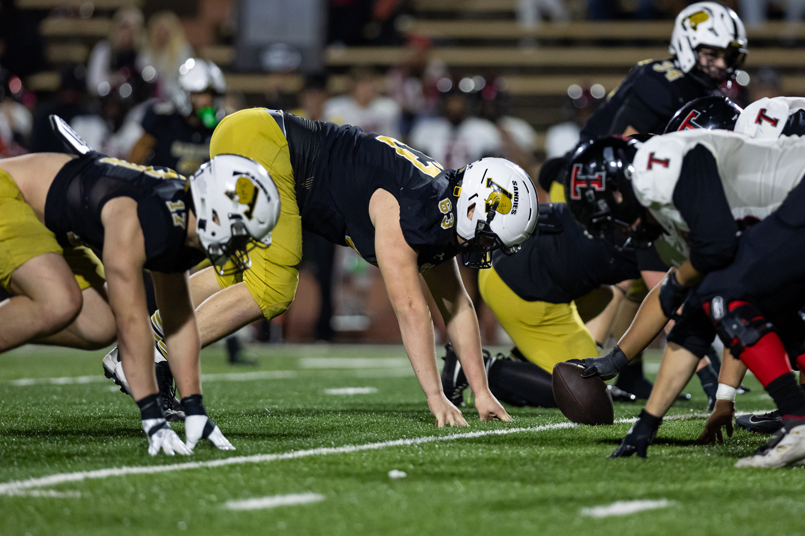 THS-AHS-FB-42 | Press Pass Sports Football players line up at the line of scrimmage before the snap, center in white helmet ready to snap the ball.