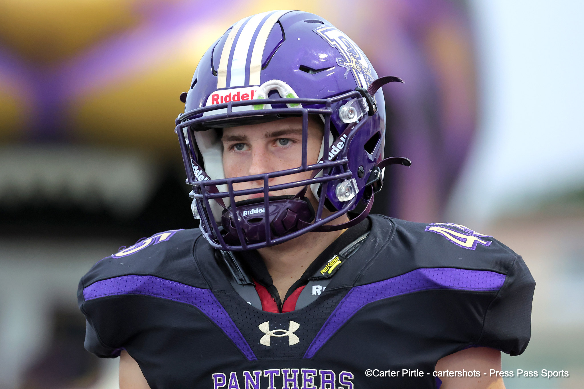 Close-up of a football player wearing a purple helmet with Panthers colors, looking off to the side.