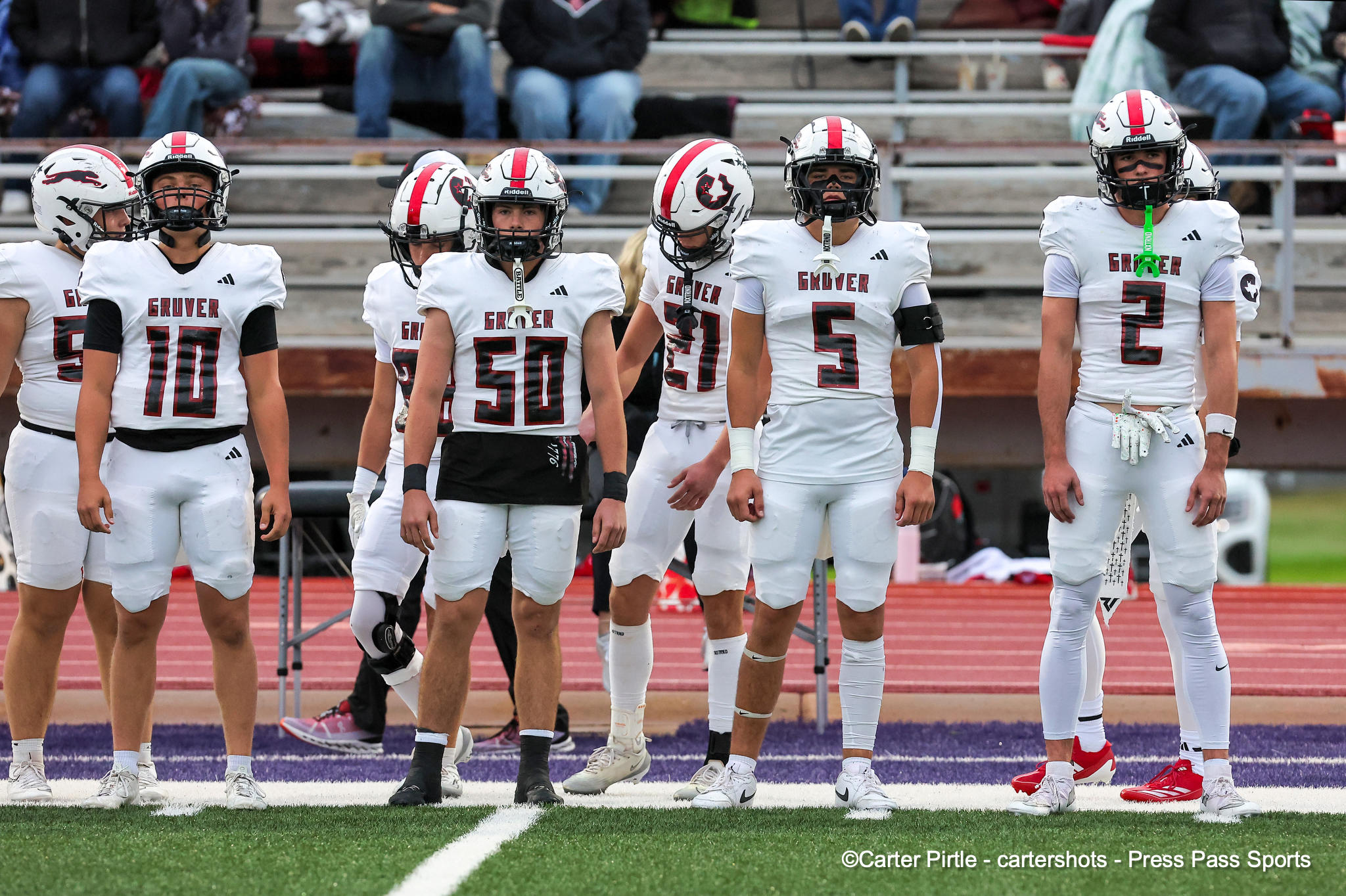 Line of football players in white uniforms standing on a track before a game, sideline scene on a sports field