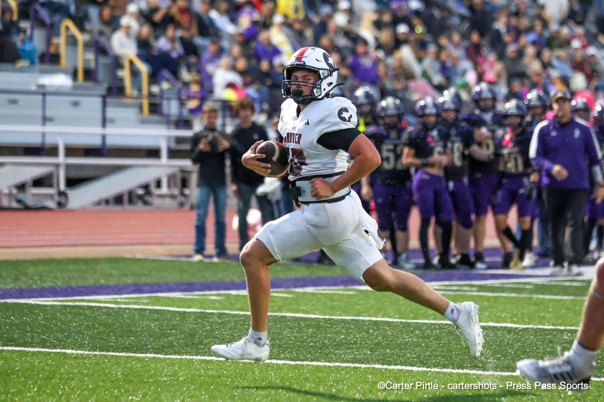 Football player in white uniform running with the ball during a game with a crowded stands in the background.