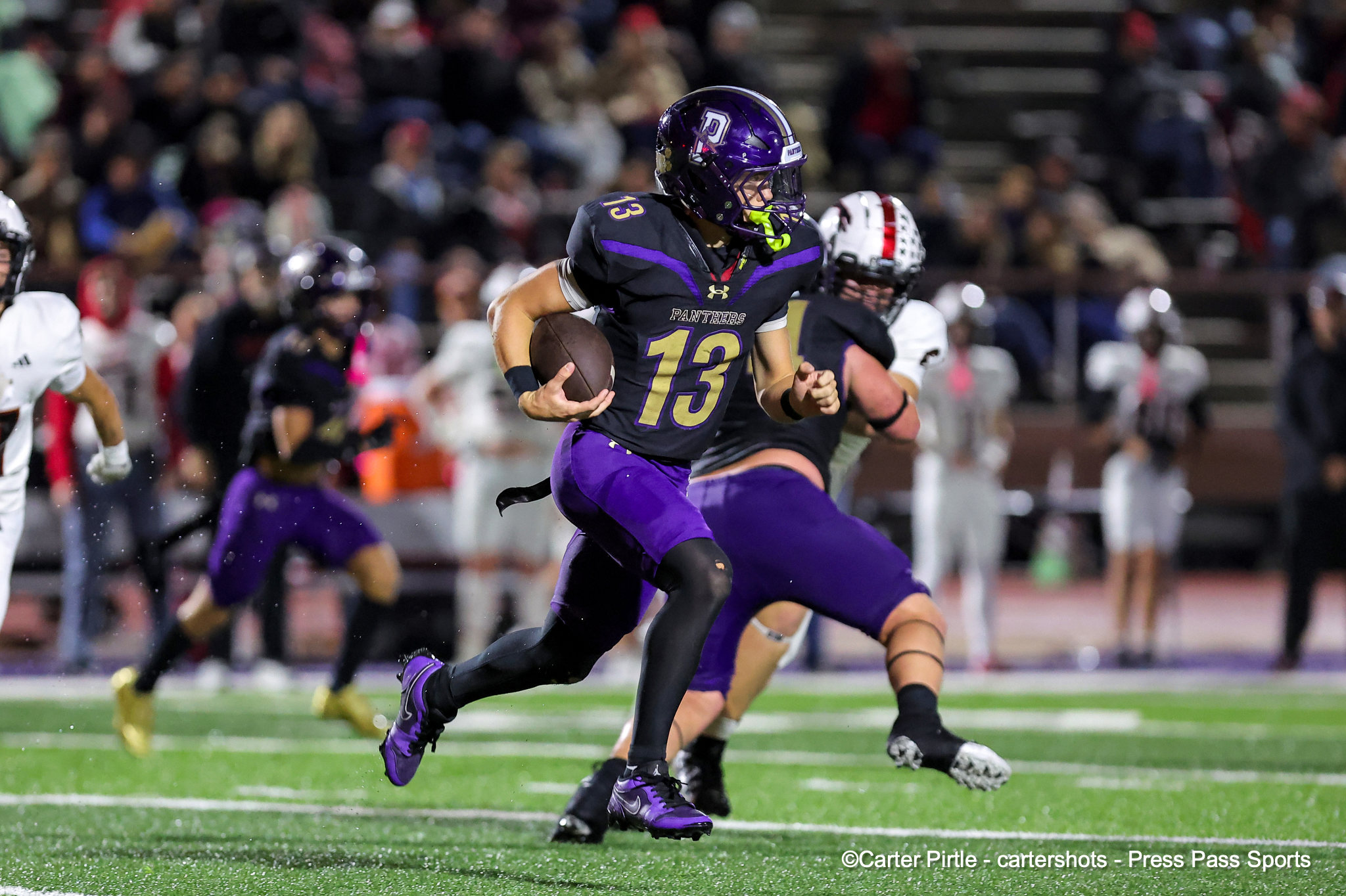 Football player in purple and gold (#13) running with the ball during a game on a lit field.