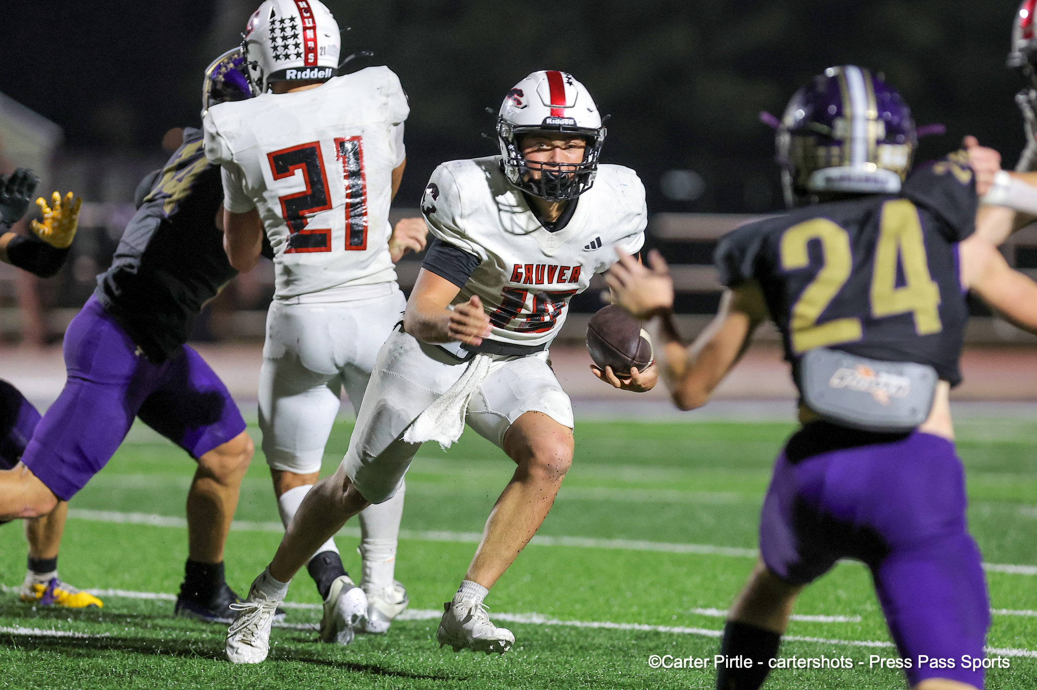 Football action: a white-jersey ball carrier races forward as purple-clad defenders close in on a green turf field at night