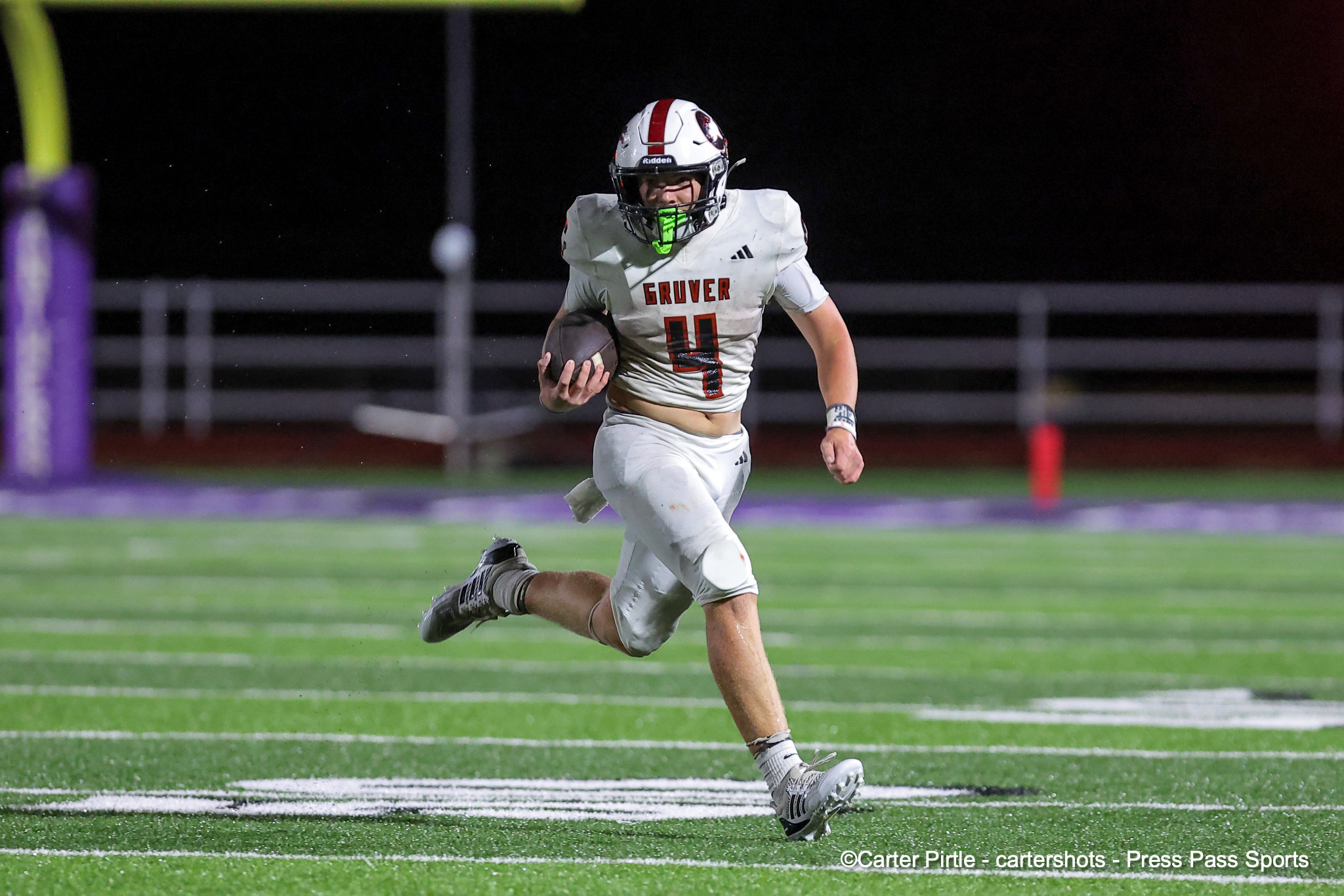 Football player in a white jersey (no. 11) runs with the ball during a night game on a green turf field.