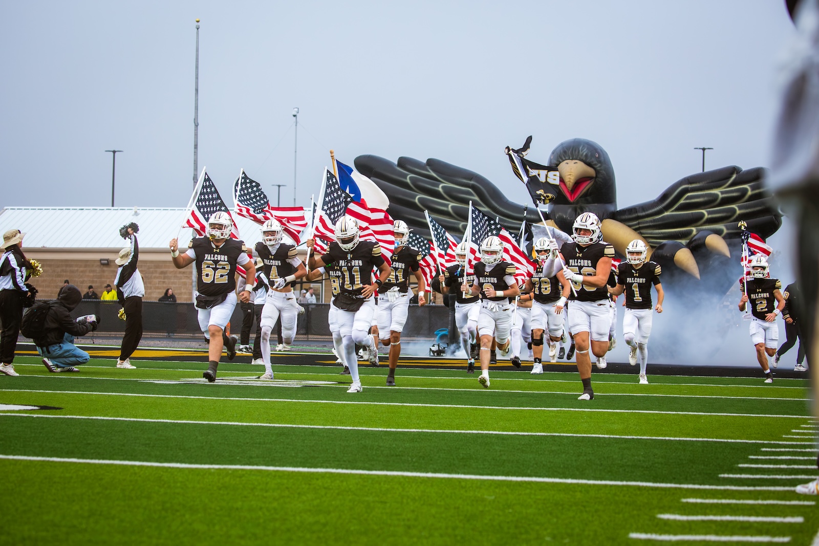 Football team runs onto the field carrying American flags with a large inflatable eagle in the background.