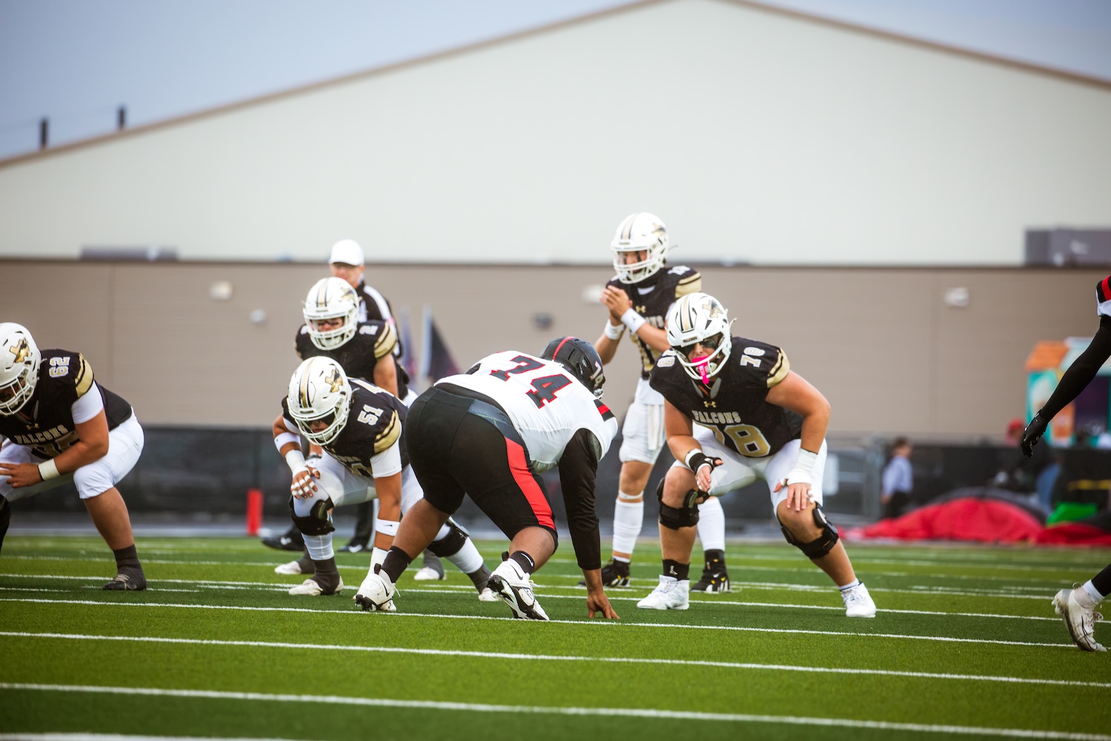 Football players line up at the line of scrimmage on a green turf field, preparing for a play.