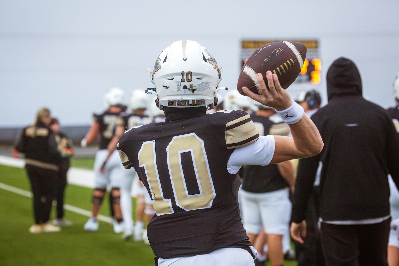 Football quarterback wearing number 10 in black and gold, about to throw a football on the sideline during a game.