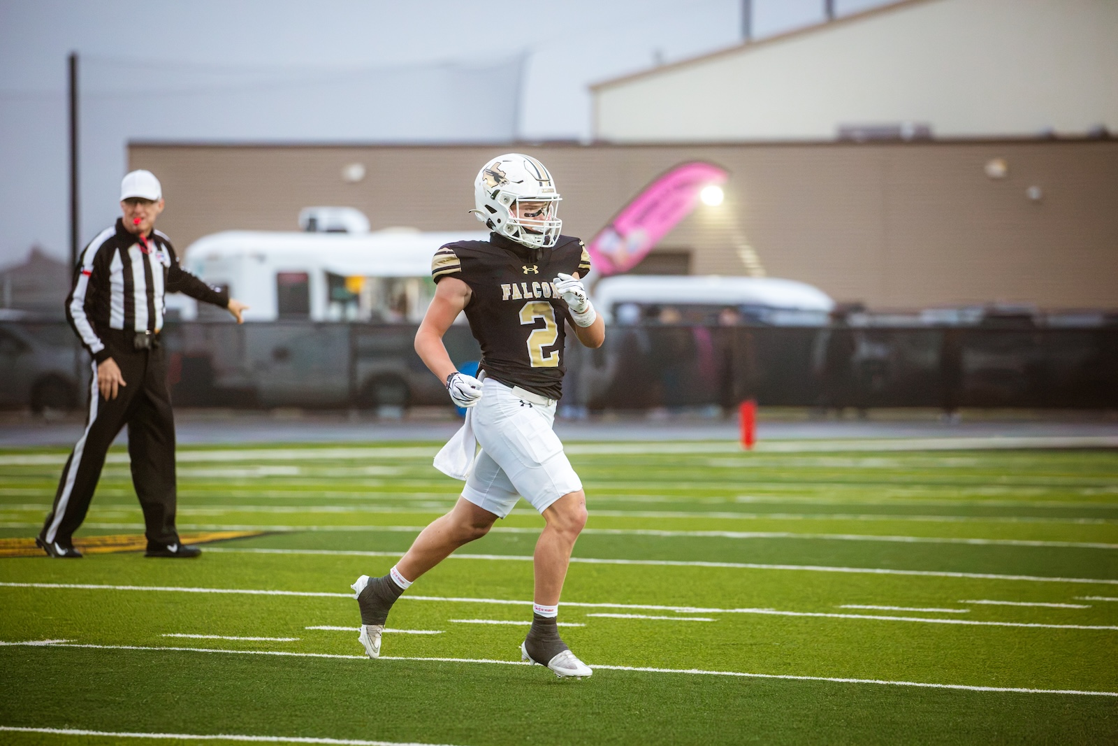 Football player in black Falcons jersey #2 running on a football field with a referee in the background as a game unfolds.