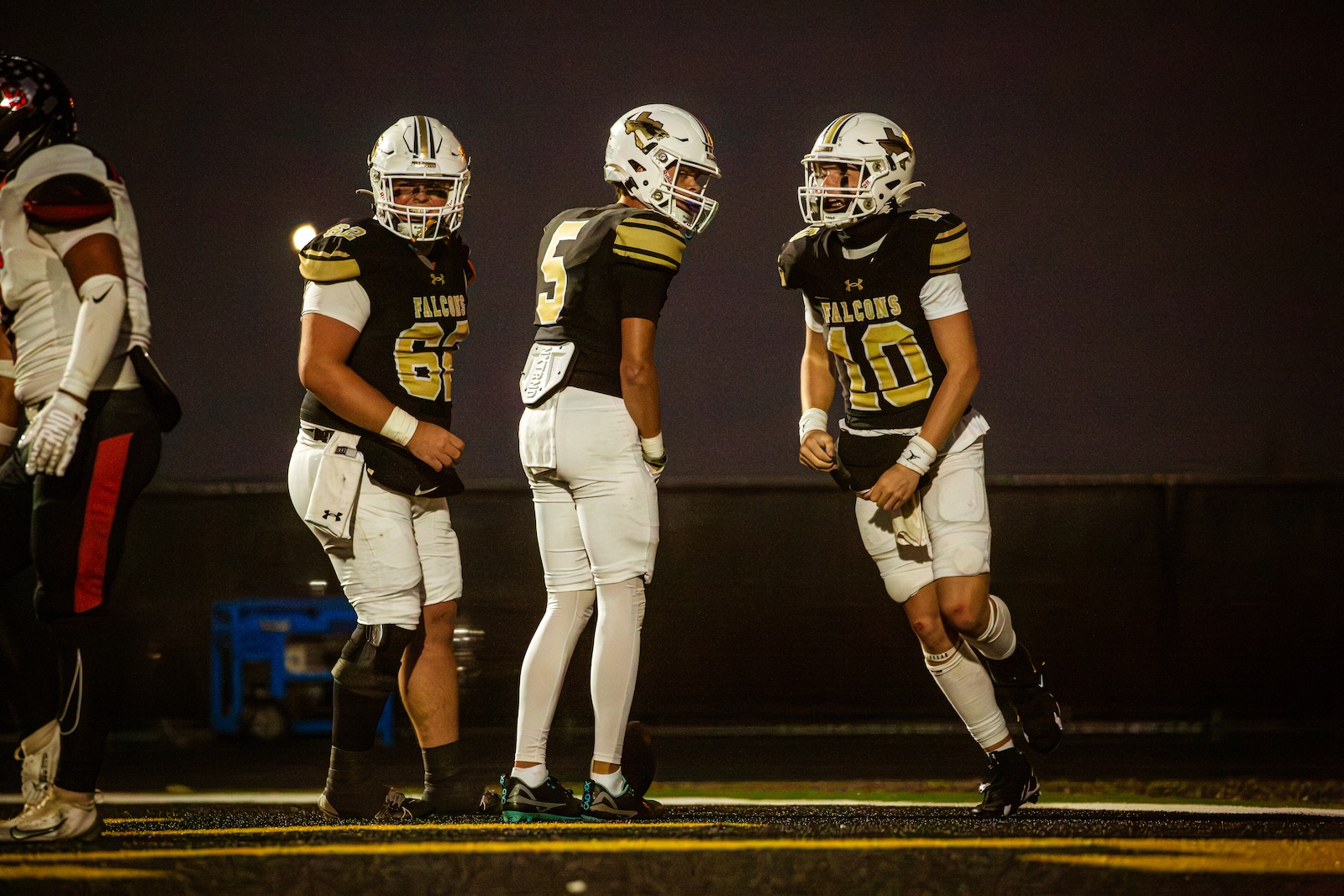 Three football players in Falcons black-and-gold uniforms stand on a dark nighttime field, preparing for play.