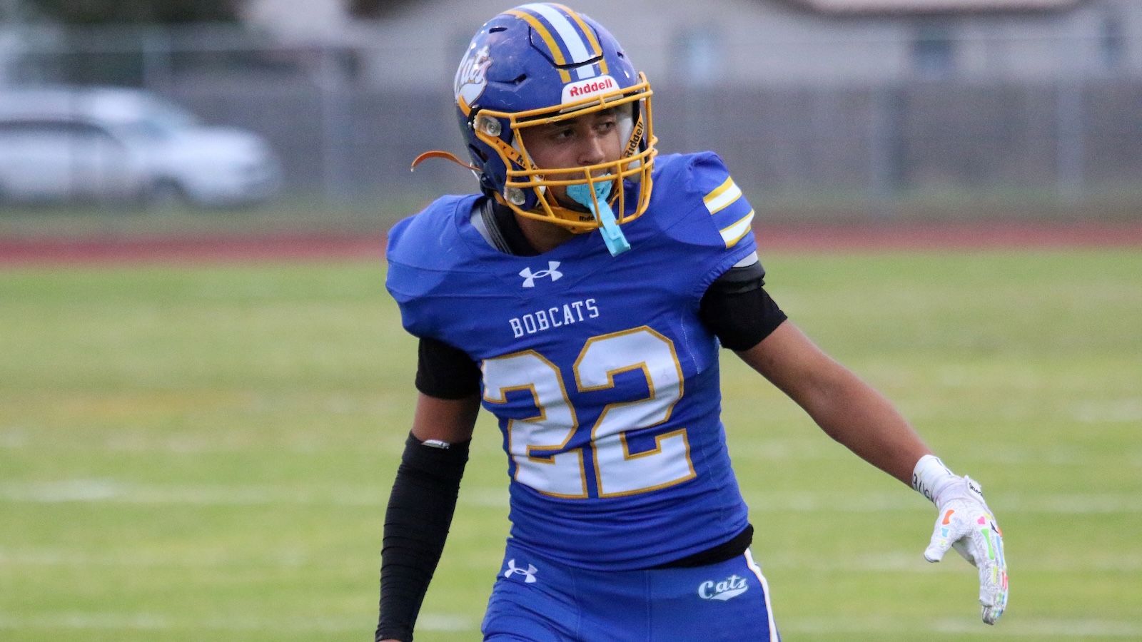 Football player wearing a blue Bobcats jersey number 22 on a grassy field, helmet with yellow face mask, mid-action pose.