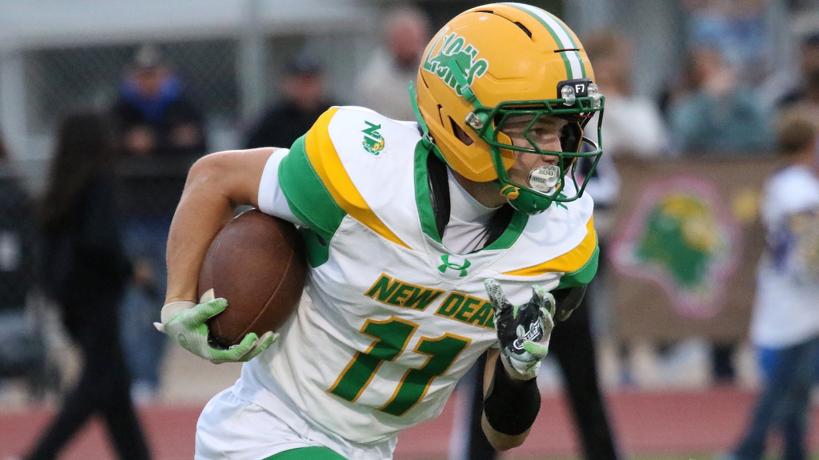Football player in a white-green-yellow New Orleans jersey (number 11) running with the ball during a game, wearing a yellow helmet and green gloves.